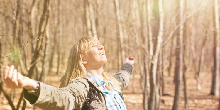 Frau genießt Sonnenstrahlen bei einer Wanderung im herbstlichen Wald