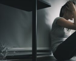 Depressive Frau sitzt auf dem Bodem im dunklen Zimmer, bedroht durch Coronaviren.