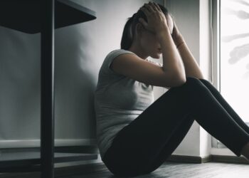 Depressive Frau sitzt auf dem Bodem im dunklen Zimmer, bedroht durch Coronaviren.