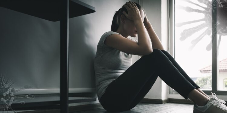 Depressive Frau sitzt auf dem Bodem im dunklen Zimmer, bedroht durch Coronaviren.
