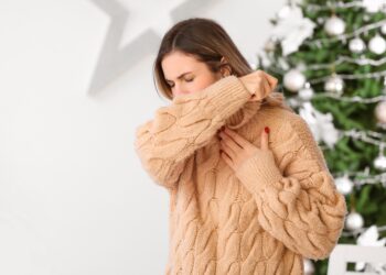 Junge Frau vor einem Weihnachtsbaum hustet in ihre Armbeuge
