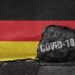 Eine Deutschlandfahne mit einem Loch in dem "COVID-19" steht.