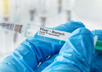 Behandschuhte Hand mit Spritze mit Impfstoff von Pfizer - Biontech