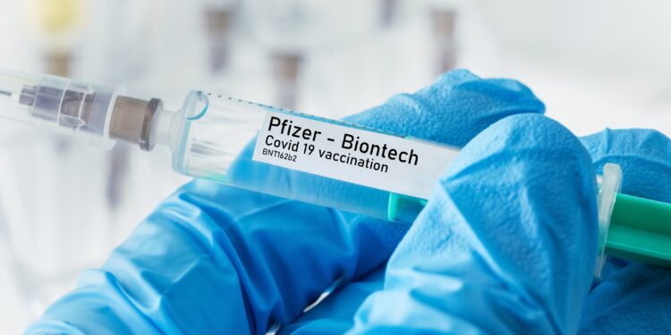 Behandschuhte Hand mit Spritze mit Impfstoff von Pfizer - Biontech