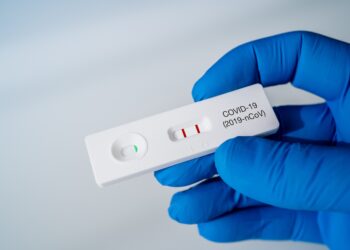 Behandschuhte Hand hält ein Testkit mit positivem Ergebnis für COVID-19