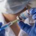 Person mit Mundschutz und blauen Handschuhen zieht einen Corona-Impfstoff in eine Spritze