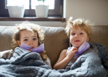 Zwei kleine kranke Kinder mit Gesichtsmaske zu Hause im Bett liegend