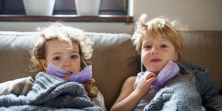 Zwei kleine kranke Kinder mit Gesichtsmaske zu Hause im Bett liegend