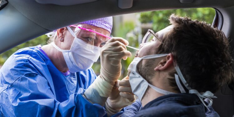 Ärztin macht bei einem im Auto sitzenden Mann einen Nasenabstrich