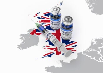 Auf einer Karte von Großbritannien liegt eine Spritze und zwei Dosen eines COVID-19-Impfstoffes.