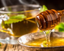 Honig und Honigschöpflöffel auf rustikalem Eichentisch und heißer Kräutertee im Hintergrund