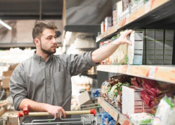 Ein Mann nimmt eine Packung Müsli aus einem Regal im Supermarkt.