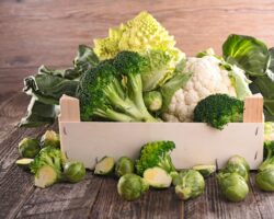 Verschiedenes Gemüse wie Brokkoli, Rosen- und Blumenkohl in einer Holzkiste und auf einem Holztisch