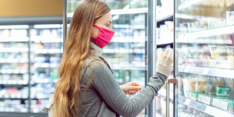 Junge Frau mit Mund-Nasen-Bedeckung beim Einkaufen im Supermarkt