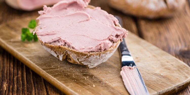 Brötchenhälfte bestrichen mit Leberwurst auf einem Brett neben einem Tafelmesser