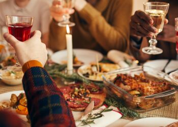 Freunde stoßen mit einem Glas Wein beim Weihnachtsessen an.