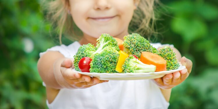 Mädchen hält einen Teller mit frischem Gemüse.