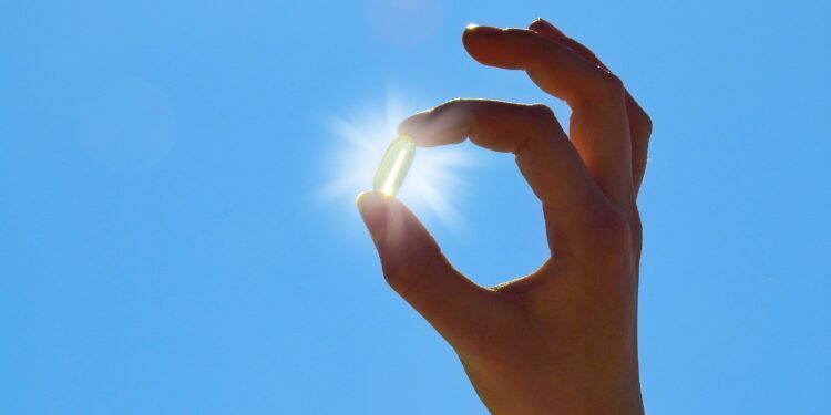 Eine Hand hält eine Pille vor die Sonne.