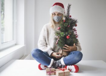 Eine Frau mit Alltagsmaske sitzt vor einem Fenster und wartet auf Weihnachten.