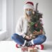 Eine Frau mit Alltagsmaske sitzt vor einem Fenster und wartet auf Weihnachten.