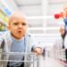 Ein Baby mit ärgerlichem Gesichtsausdruck sitzt in einem Einkaufswagen im Supermarkt.