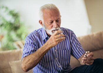 Auf dem Sofa sitzender Senior nimmt eine Tablette ein