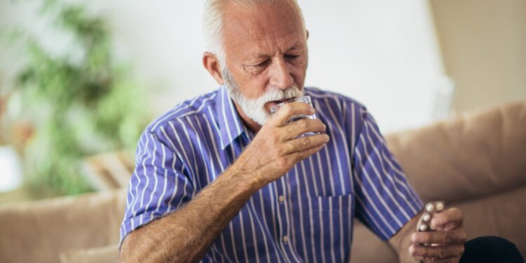 Auf dem Sofa sitzender Senior nimmt eine Tablette ein