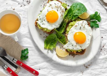 Gebratene Eier auf Brotscheiben mit Avocado neben einer Tasse Tee