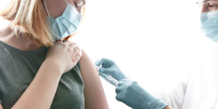 Frau mit Mund-Nasenbedeckung wird von einer Ärztin geimpft