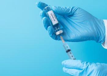 Behandschuhte Hände ziehen Impfstoff aus einer Ampulle in eine Spritze