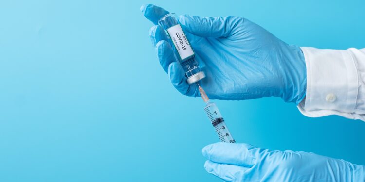 Behandschuhte Hände ziehen Impfstoff aus einer Ampulle in eine Spritze