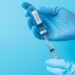 Behandschuhte Hände ziehen Impfstoff aus einer Ampulle in eine Spritze