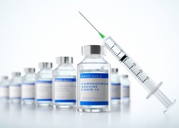 Eine Spritze lehnt an Glasfläschchen mit der Aufschrift: Coronavirus Vaccine COVID-19.