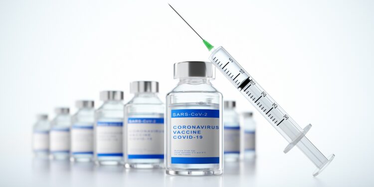 Eine Spritze lehnt an Glasfläschchen mit der Aufschrift: Coronavirus Vaccine COVID-19.