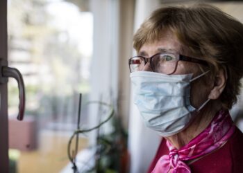 Seniorin mit Mundschutz schaut aus dem Fenster