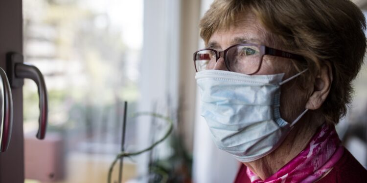 Seniorin mit Mundschutz schaut aus dem Fenster