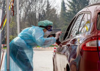 Krankenschwester nimmt bei einer im Auto sitzenden Person einen Abstrich für einen Coronavirus-Test