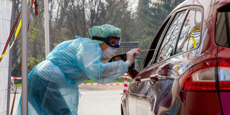 Krankenschwester nimmt bei einer im Auto sitzenden Person einen Abstrich für einen Coronavirus-Test