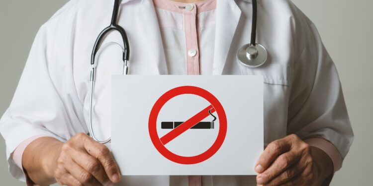 Arzt mit umgehängtem Stethoskop hält ein Nichtrauchen-Schild