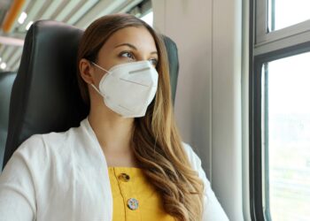 Frau mit FFP2-Maske in einem Zug sieht aus dem Fenster