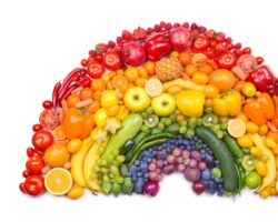 Verschiedenfarbige Obst und Gemüsesorten sind in Form eines Regenbogens angeordnet.