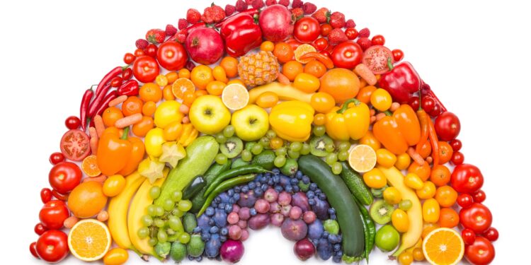 Verschiedenfarbige Obst und Gemüsesorten sind in Form eines Regenbogens angeordnet.