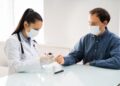 Ärztin mit Maske checkt Blutzucker von einem Patienten mit Maske