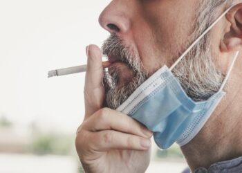 Ein Mann mit heruntergezogener Gesichtsmaske raucht eine Zigarette.