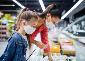 Mutter und Tochter mit Mund-Nasen-Bedeckung beim Einkaufen im Supermarkt