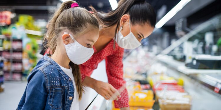 Mutter und Tochter mit Mund-Nasen-Bedeckung beim Einkaufen im Supermarkt