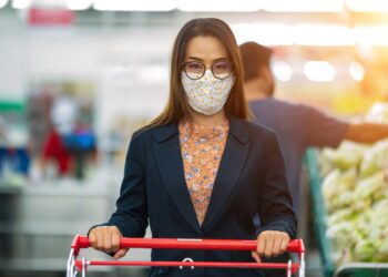 Eine Frau mit Mund-Nasen-Bedeckung mit einem Einkaufswagen im Supermarkt