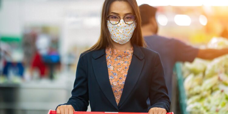 Eine Frau mit Mund-Nasen-Bedeckung mit einem Einkaufswagen im Supermarkt