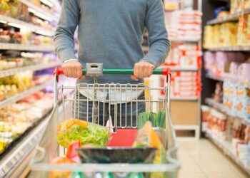 Mann beim Einkaufen im Supermarkt mit vollem Einkaufswagen