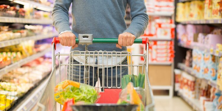 Mann beim Einkaufen im Supermarkt mit vollem Einkaufswagen